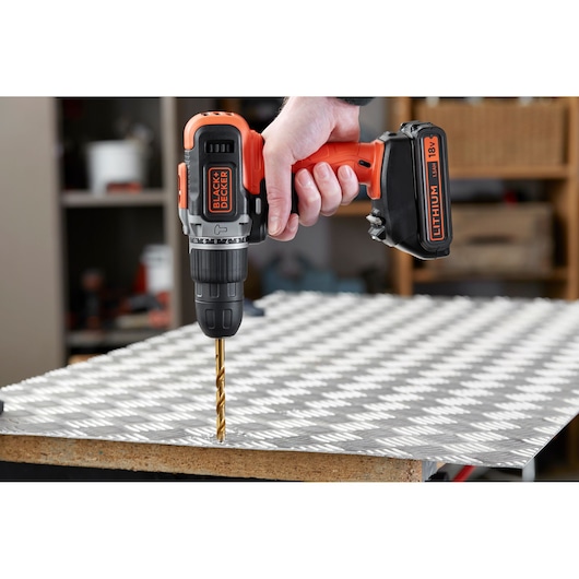 Photo of BLACKDECKER BCD003C1 cordless drill in use, drilling metal sheet, close-up side angle.