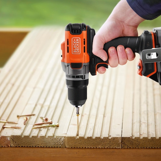 BLACK+DECKER BCD382D1 cordless drill being used to drive a screw into wood with scattered screws nearby.