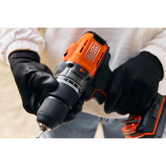 Photo of BLACKDECKER BCD383D1 cordless drill, orange and black, held by gloved hands.