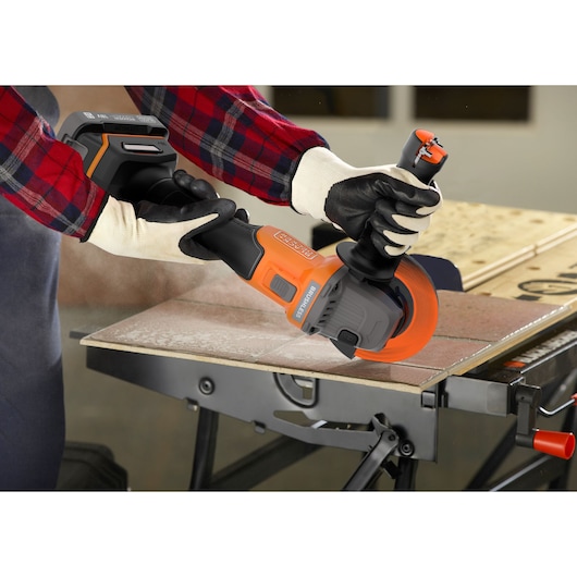 Photo of BLACKDECKER BCG6L8D1S cordless angle grinder in use cutting tile, user wearing gloves and plaid shirt.