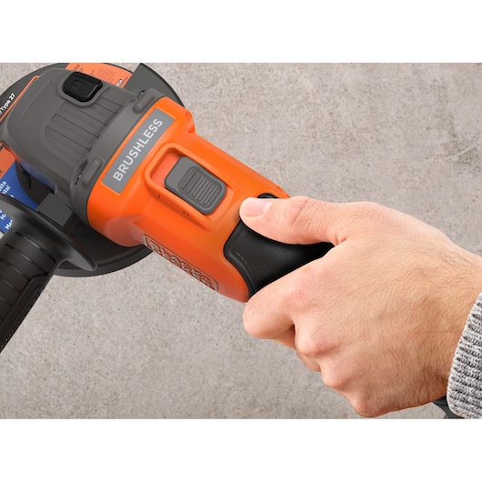 Photo of a hand holding a BLACK+DECKER BCG6L8D1S cordless brushless angle grinder, close-up on power switch.