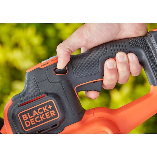 Close-up of a hand holding BLACK+DECKER BCHTS3620L1 power tool handle with textured grip and visible trigger, outdoors.