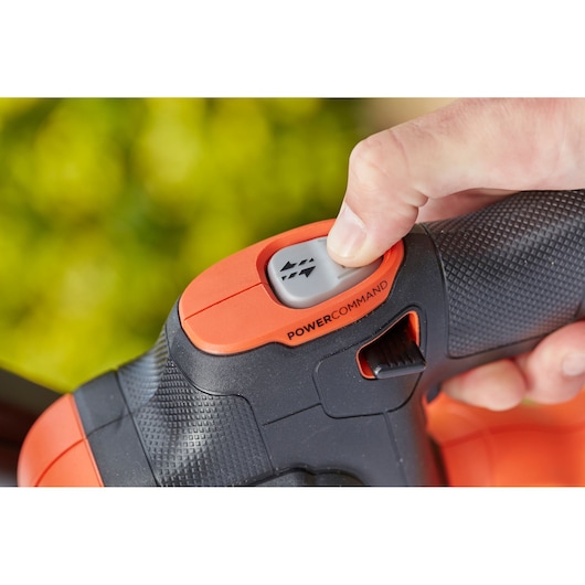 Close-up photo of hand pressing POWERCOMMAND button on BLACKDECKER hedge trimmer handle BCHTS3620L1.