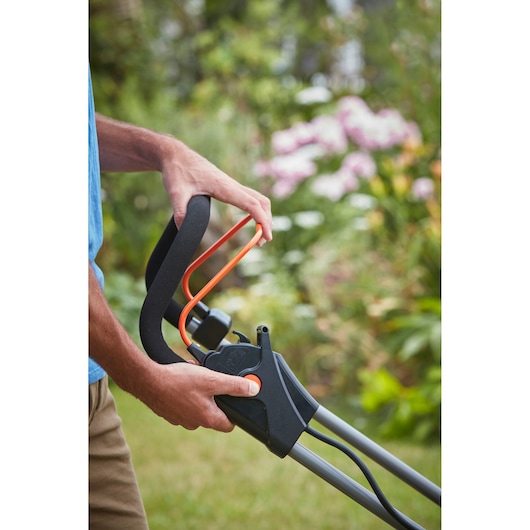 Close-up of BLACKDECKER BCMW3318N lawn mower handle with operator hands in a garden setting.