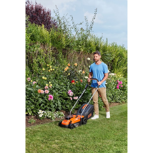 Photo of BLACKDECKER BCMW33362L1 lawn mower in use on grass near flower garden.