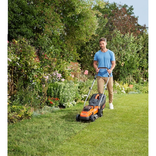 Photo of BLACKDECKER BCMW33362L1 lawn mower being used in a garden with green grass and flowers.