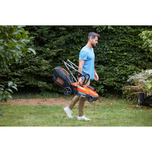Photo of BLACKDECKER BCMW33362L1 lawn mower being carried by a person in a garden.