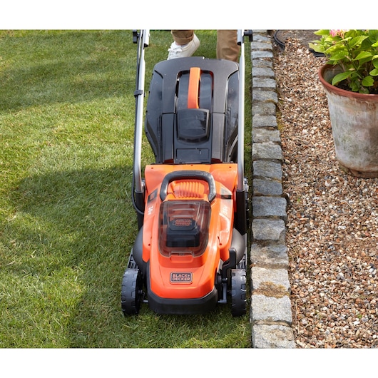 Photo of BLACK+DECKER BCMW33362L1 cordless lawn mower on grass, front view, orange and black color.