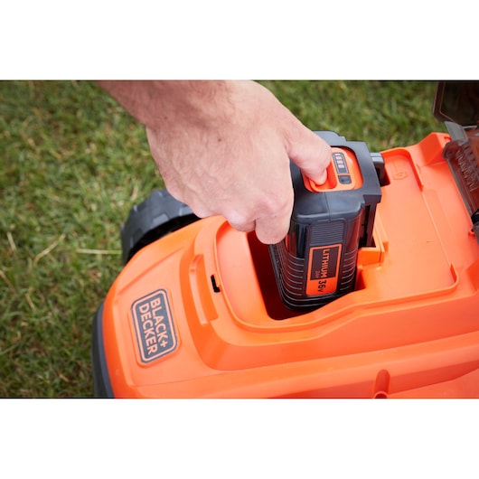 Close-up photo of a BLACK+DECKER lawn mower BCMW33362L1 with a hand inserting a lithium battery.