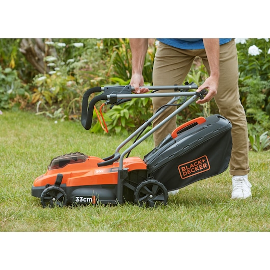 Photo of BLACKDECKER BCMW33362L1 cordless lawn mower, orange and black, on grass in a garden setting.