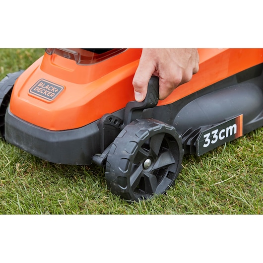 Close-up photo of BLACK+DECKER BCMW33362L1 lawn mower wheel and height adjustment lever on grass.