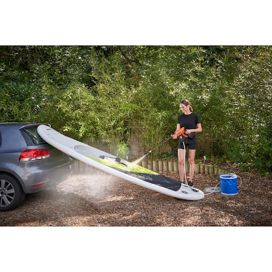 BLACKDECKER BCPC18B portable pressure washer cleaning a paddleboard outside, person holding sprayer, car nearby.