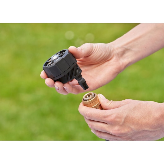 Photo of hands connecting BLACKDECKER BCPC18D1 pressure washer nozzle and brass hose connector outdoors.