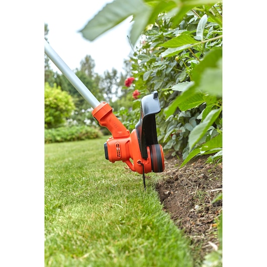 BLACKDECKER BCSTA536B grass trimmer close-up cutting lawn edge near garden plants outdoors.