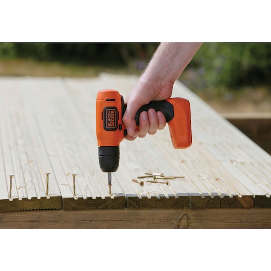 Photo of BLACK+DECKER BDCD8 cordless drill being used to drive a screw into wood, outdoor setting.