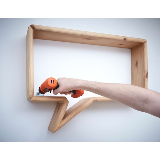 BLACKDECKER BDCD8 cordless drill used to mount wooden shelf on wall, close-up of tool in action