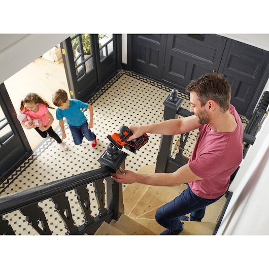 BLACKDECKER BDCDS18 cordless sander in use on black staircase railing inside a home.