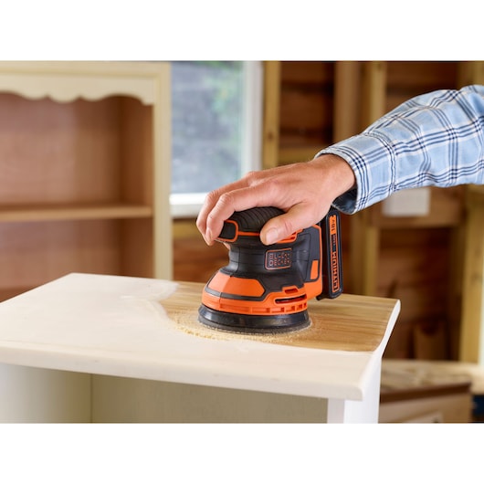 BLACKDECKER BDCROS18N cordless random orbital sander being used on wooden furniture.