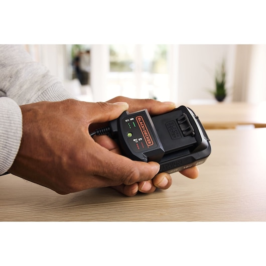 Photo of BLACK+DECKER BDL2018S1B battery charger in hand on table, compact design with LED indicator lights.