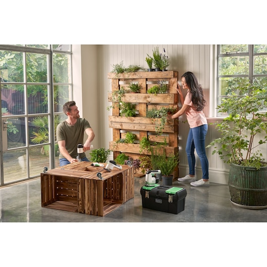BLACKDECKER BDST60120 black tool box with green latches on floor, indoor gardening scene with wood pallet planter.