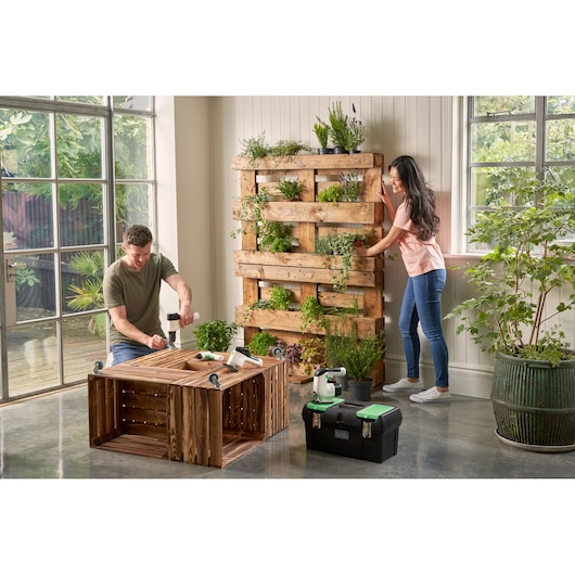 BLACKDECKER BDST60120 black toolbox with green latches on floor, shown in indoor gardening workspace.