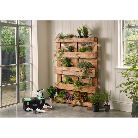 BLACKDECKER BDST60120 toolbox with green lid, compact tools, and a vertical garden pallet, indoor setting, front angle.