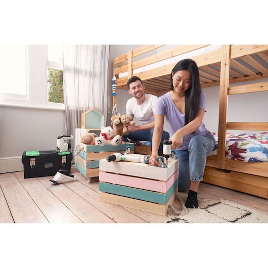 BLACKDECKER BDST60120 tool box and tools on wooden floor, with people assembling colorful storage crates in a children's room.