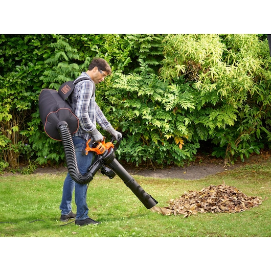 BLACKDECKER BEBLV300 leaf blower with collection bag in use in a garden clearing dry leaves.