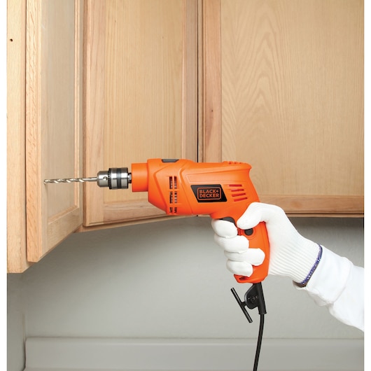Photo of BLACKDECKER BEH201 corded orange drill used on a wooden cabinet, held by a gloved hand.