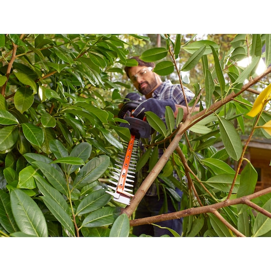 BLACKDECKER BEHTS501 hedge trimmer in use cutting green branches outdoors.