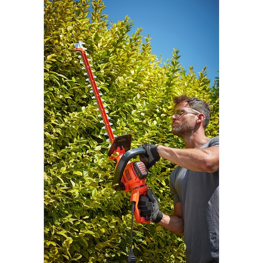 BLACKDECKER BEHTS551 hedge trimmer in use trimming green bushes outdoors.