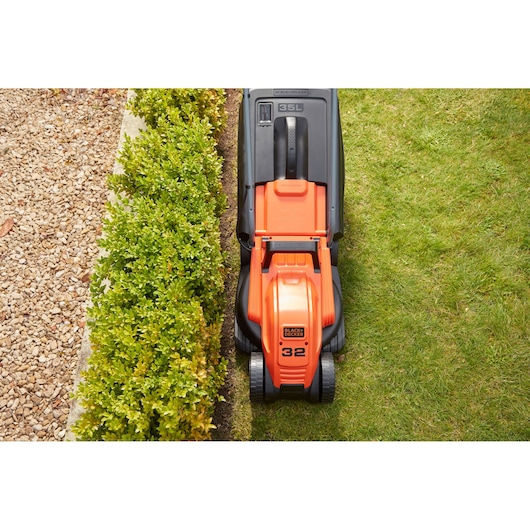 BLACK+DECKER BEMW451 lawn mower top view cutting grass along garden edge.