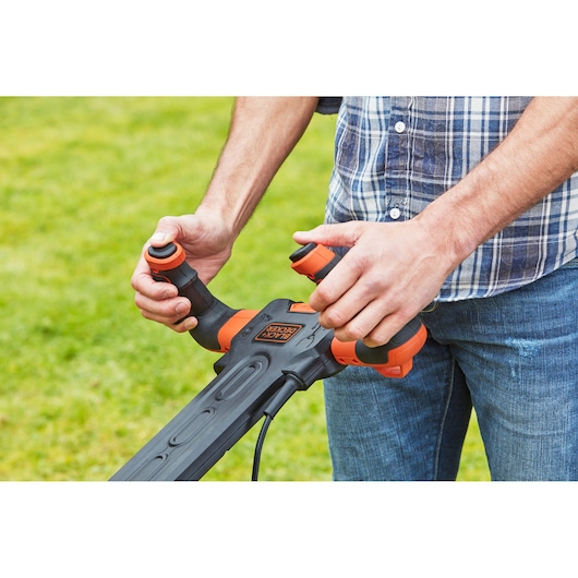 Photo of hands operating BLACK+DECKER BEMW471ES lawn mower ergonomic handle outdoors.