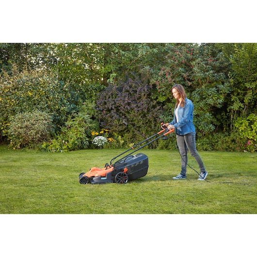 Photo of BLACKDECKER BEMW481BH lawn mower in use on grass, pushed by a person, with garden background.