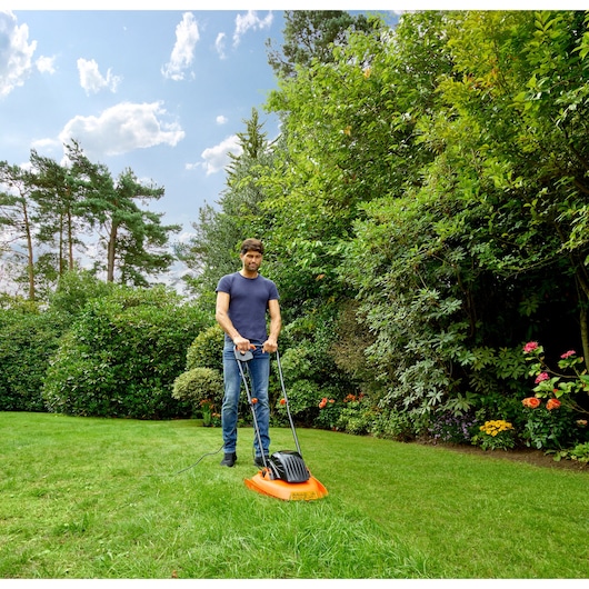 BLACKDECKER BEMWH551 orange hover lawn mower in use on a garden lawn on a sunny day