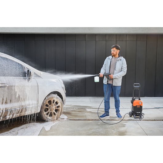 BLACKDECKER BEPW2000 pressure washer spraying foam on a dirty car outdoors.