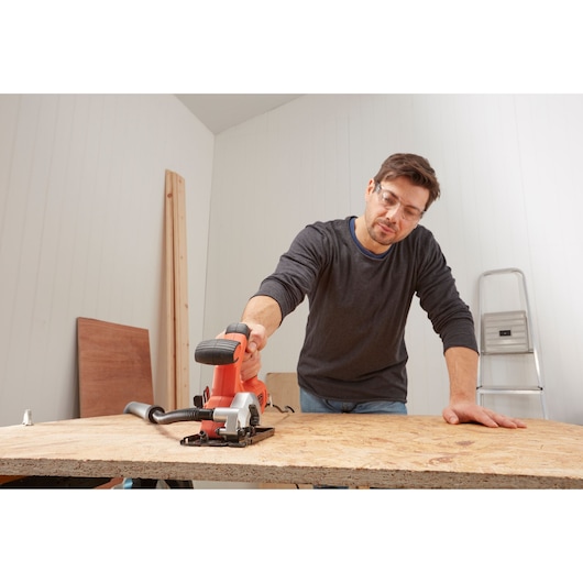 Photo of a person using a BLACKDECKER BES510 compact circular saw to cut wood on a workbench indoors.
