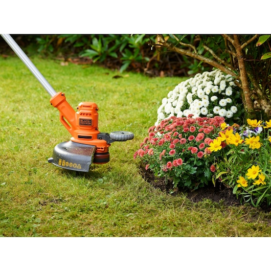 BLACKDECKER BESTA530CM grass trimmer in use near flower beds on lawn, side angle photo.