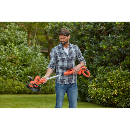 BLACKDECKER BESTA530CM orange grass trimmer held outdoors by person wearing plaid shirt.