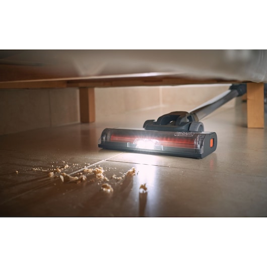 BLACKDECKER BHFEA520J stick vacuum cleaning crumbs from tile floor under furniture, LED light illuminated.