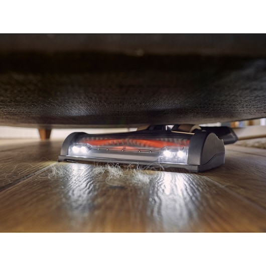 BLACKDECKER BHFEV36B2D cordless vacuum cleaning under furniture with LED lights, pet hair visible on wooden floor.