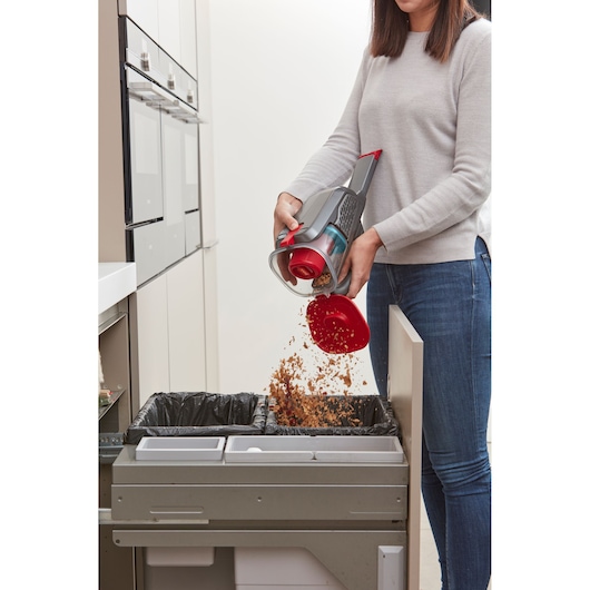 BLACKDECKER BHHV315J handheld vacuum being emptied into kitchen trash bin.