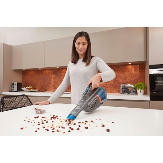 BLACKDECKER BHHV320B handheld vacuum cleaning crumbs from a kitchen countertop.