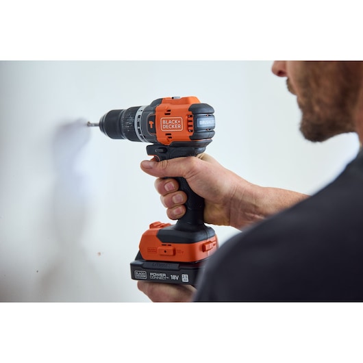 Photo of BLACK+DECKER BLD783E1K cordless drill in use on a white wall, orange and black design.
