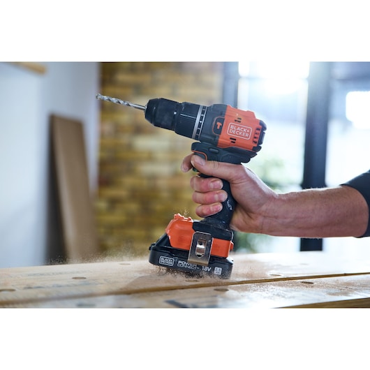 Photo of BLACK+DECKER BLD783E1K cordless drill in use, orange and black, drilling wood indoors.