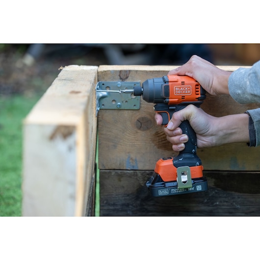 Photo of BLACK+DECKER cordless impact driver BLIM78N in use, driving screw into wooden structure outdoors.