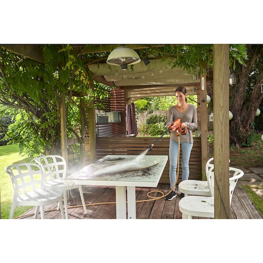 BLACKDECKER BZO51N1 pressure washer cleaning outdoor table on wooden patio surrounded by white chairs.