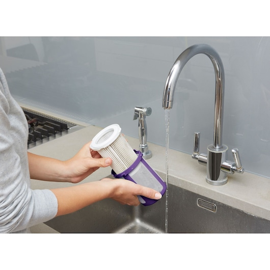 BLACKDECKER CUA525BHP vacuum filter being rinsed under a kitchen faucet, close-up photography.
