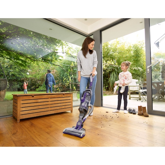 Photo of BLACKDECKER CUA525BHP cordless vacuum cleaner being used on a hardwood floor indoors, family in the background.
