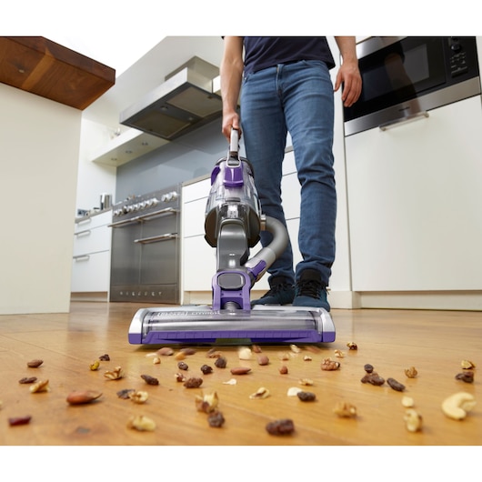 BLACKDECKER CUA525BHP vacuum cleaner in use cleaning nuts on kitchen floor, front angle.